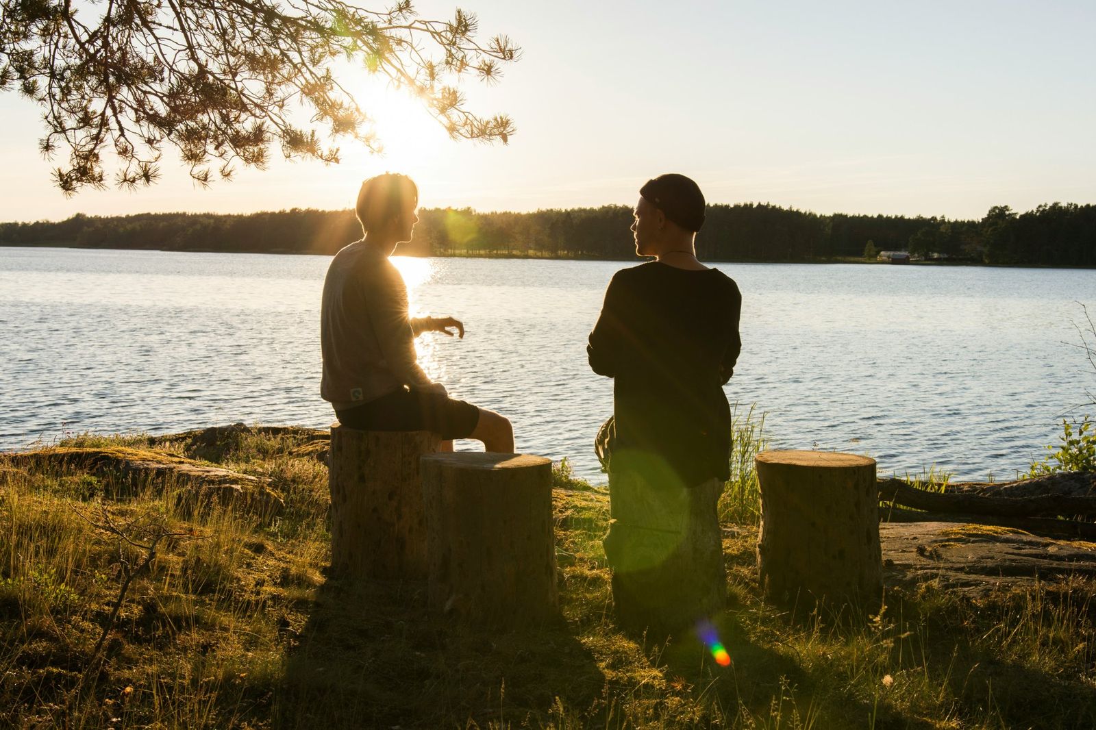 Two people sitting by a lake at sunset, having a calm conversation