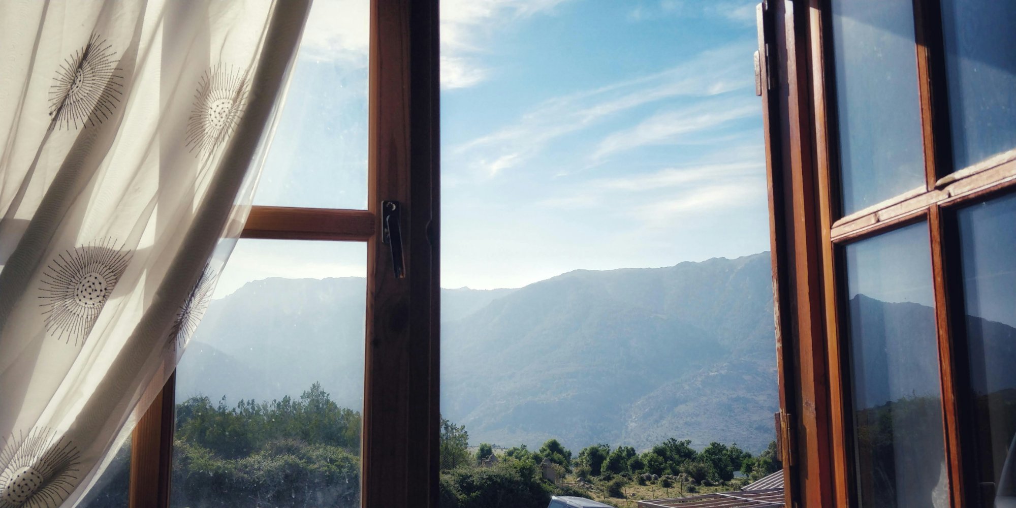 Open window with sheer curtain blowing in the breeze, mountains in the distance