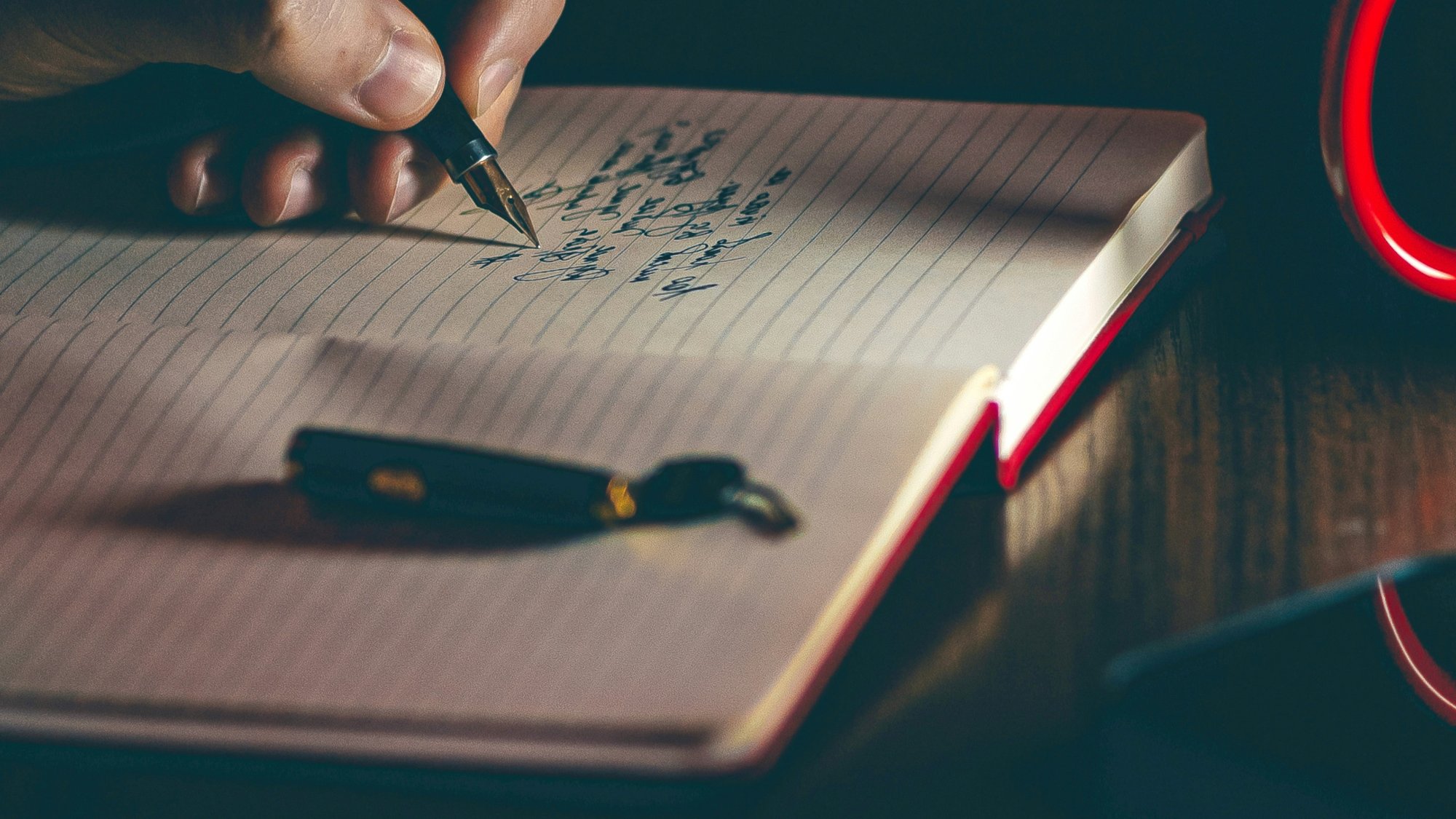 Close-up of a hand writing with a fountain pen in a lined notebook