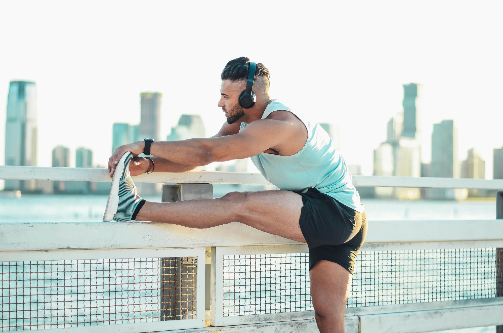 Man stretching his leg on a railing with headphones on, city skyline in the background