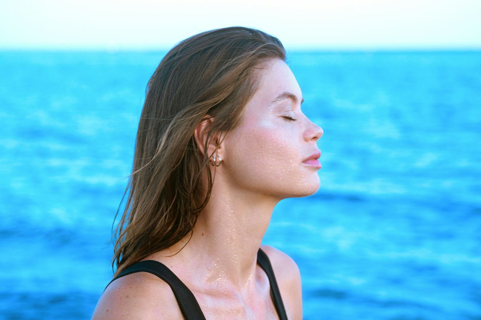 Woman with eyes closed by the ocean, face relaxed, breathing calmly, illustrating the soft quality of breath in yin yoga